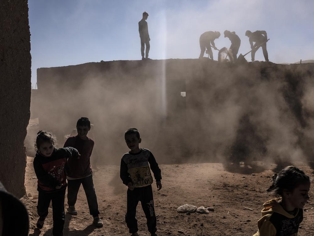 Syrian children play while adults are on the roof dismantling a house at the Rukban camp for displaced people in southern Syria, Dec. 14.