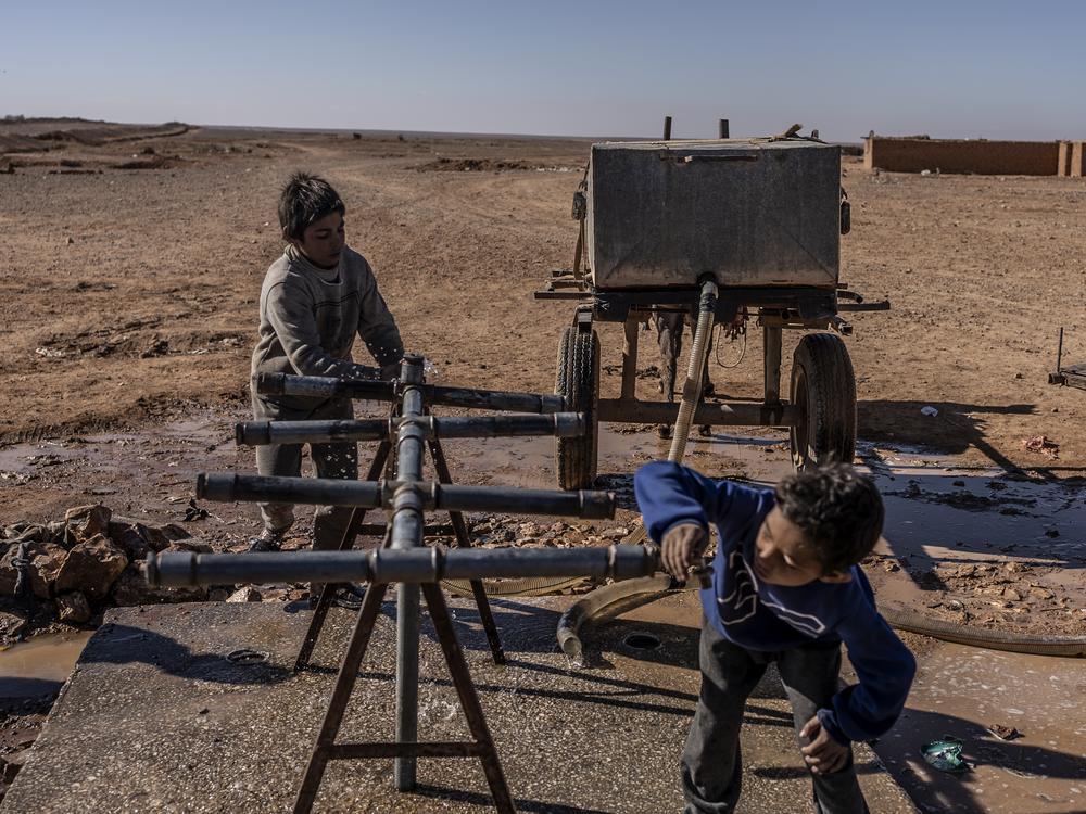 A child drinks water while another fills water in a jerry can on a cart pulled by a donkey at one of the fountains located on the edge of Rukban camp, near the southern Syrian border, Dec. 14.