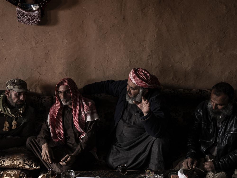 Fawaz al-Taleb gestures as he speaks with other Syrian men gathered in the living room of a home in the Rukban camp for displaced people, on Dec. 14.