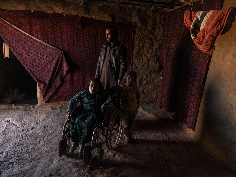 She'ala Hjab Khaled sits in a wheelchair, with her father and sister standing with her, in their house in the Rukban camp for displaced people in southern Syria, Dec. 14.