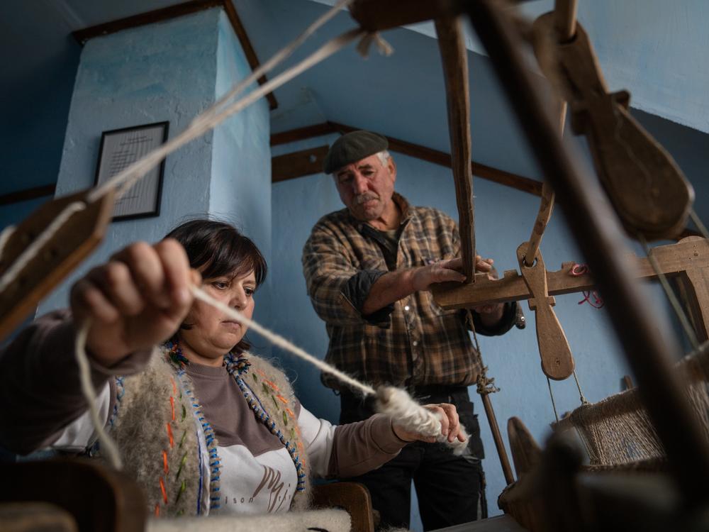 Lubov Hychka demonstrates how to weave the hunia fabric while Vasyl Hychka (unrelated), who takes care of the property where the loom is housed, helps with the rickety old machine.