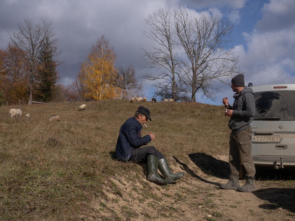 Mikhailo Bilak sits to smoke a cigarette after walking all morning with his flock of sheep. Mykola Yakbuk (right) has come to take one of the ewes and her lambs back to a barn where they can be more closely cared for.