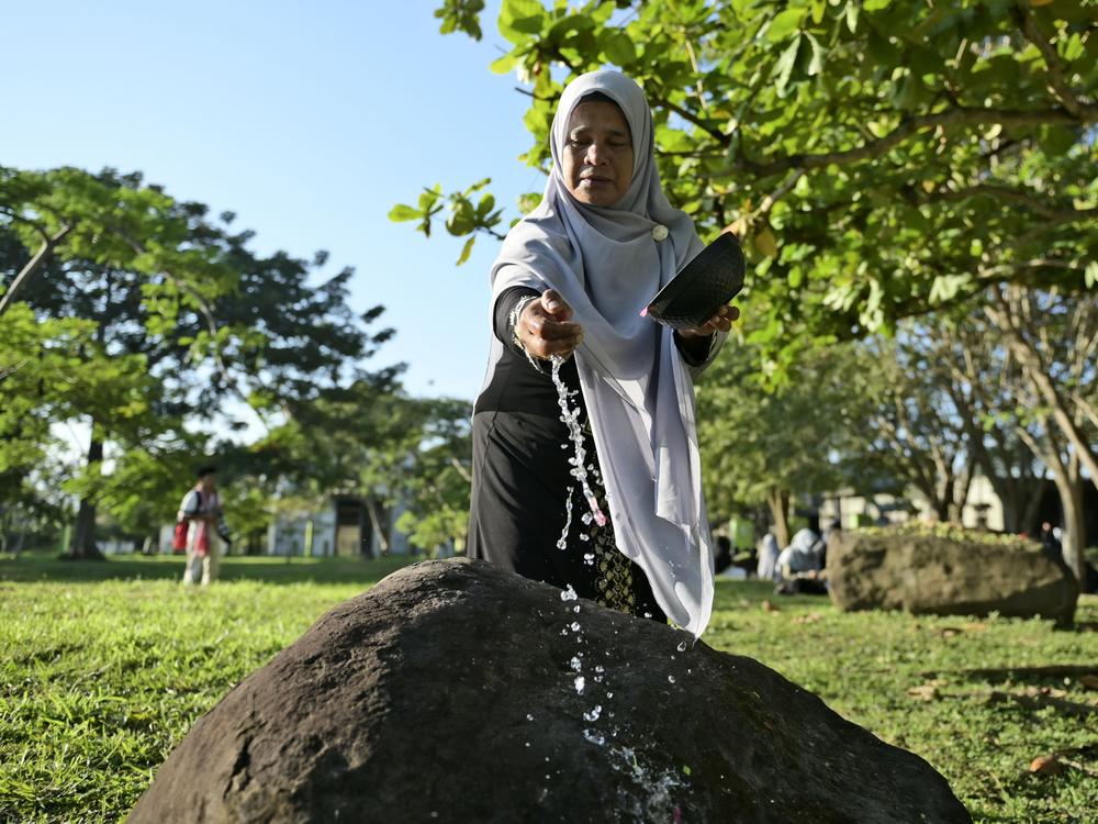 A woman sprinkles water on a stone marking a mass grave of victims of the 2004 Indian Ocean tsunami in Banda Aceh, Indonesia, on Thursday.