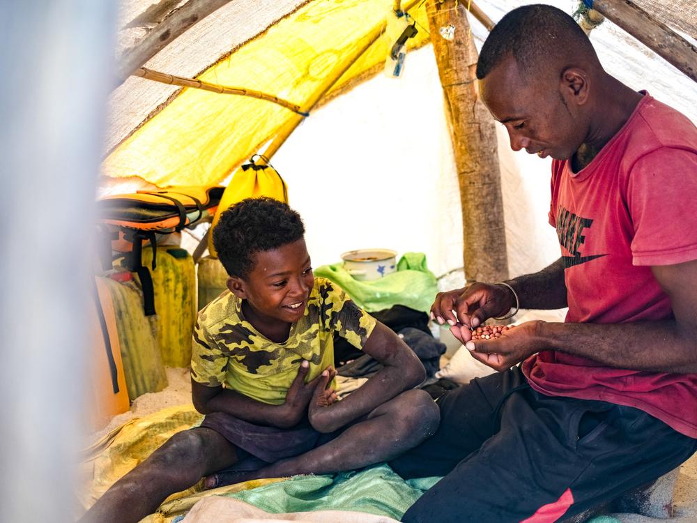 Migrant Vezo fisherman Netson Kassim, 30, shares peanuts with his son in the tent they live in for 9 months a year.