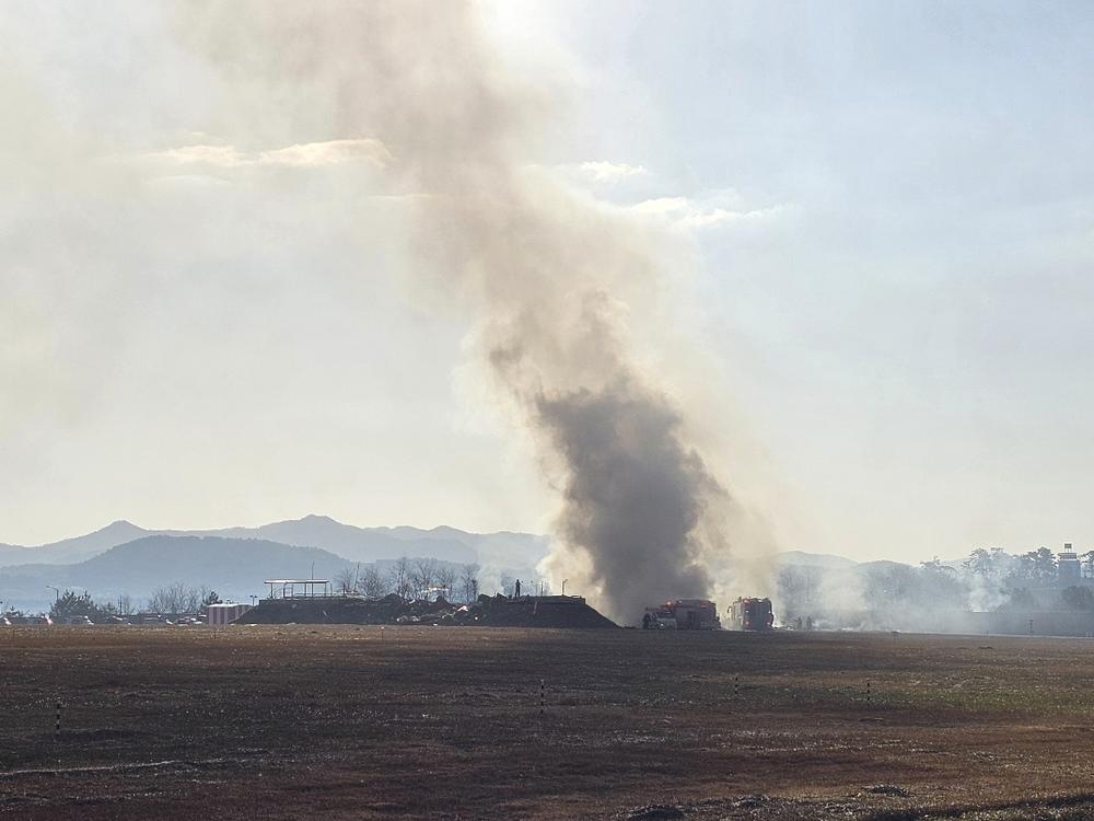 Firefighters work to extinguish a fire off the runway of Muan International Airport in Muan, South Korea, Sunday. (Maeng Dae-hwan/Newsis via AP)
