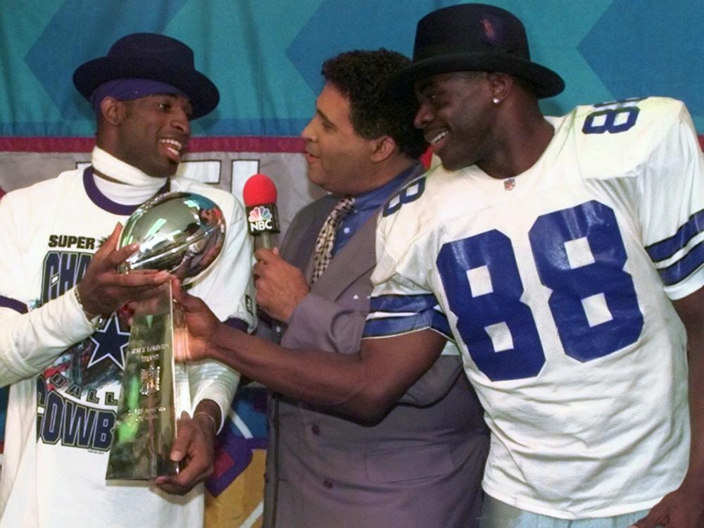 Dallas Cowboys cornerback Deion Sanders (left) and running back Michael Irvin (88) share the Vince Lombardi trophy as NBC commentator Greg Gumbel interviews the two after Super Bowl XXX in Tempe, Ariz., on Jan. 28, 1996.