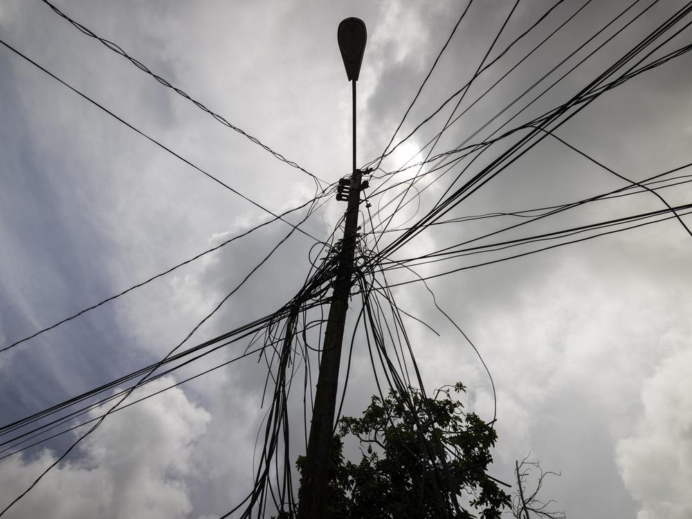 A utility pole with loose cables is shown towering over a home in Loiza, Puerto Rico, Sept. 15, 2022.