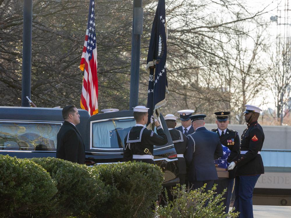 Military members transfer the casket of former U.S. President Jimmy Carter from the hearse into the Carter Center.