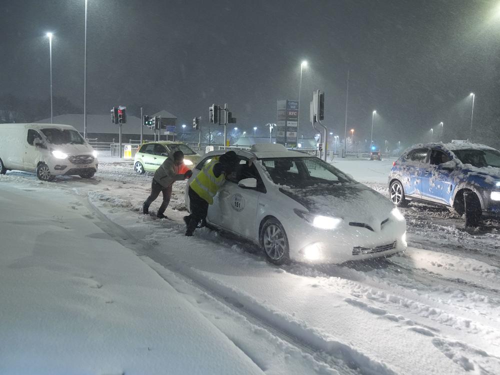 People help to push cars stuck in snow in Leeds, England, Sunday, Jan. 5, 2025.