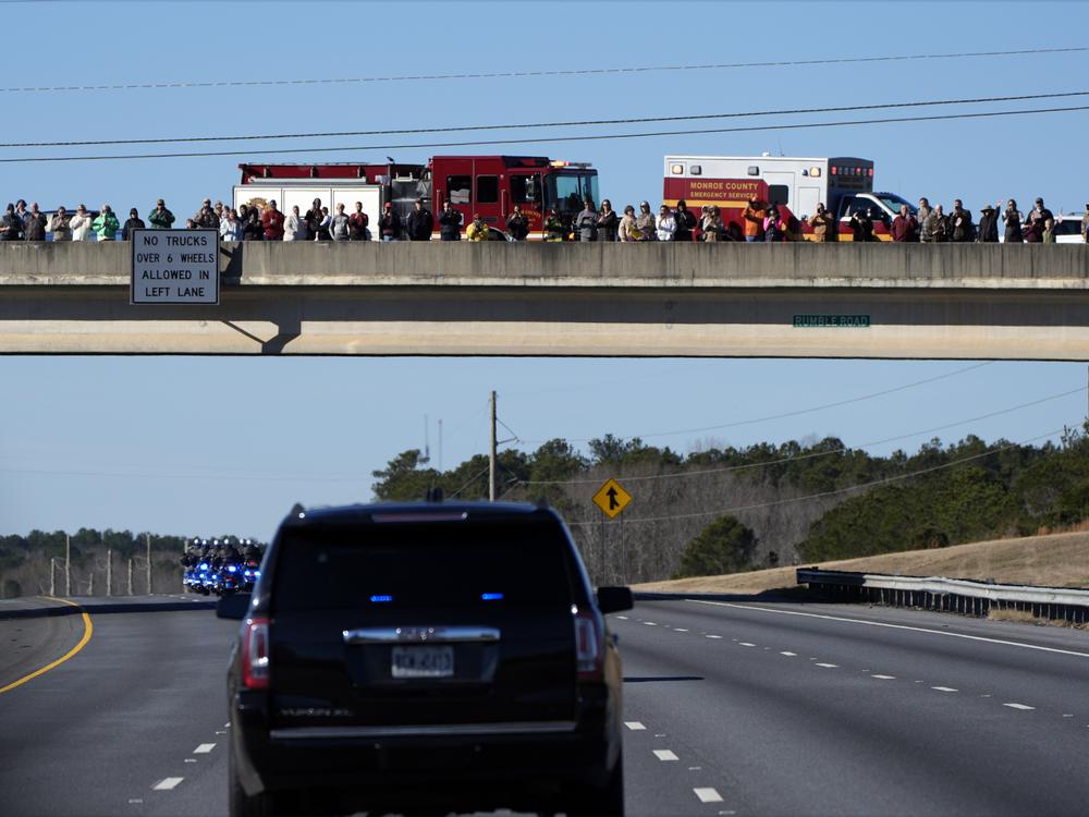 People watch from an overpass as the hearse containing the casket of former President Jimmy Carter drives on I-75 en route to Atlanta.