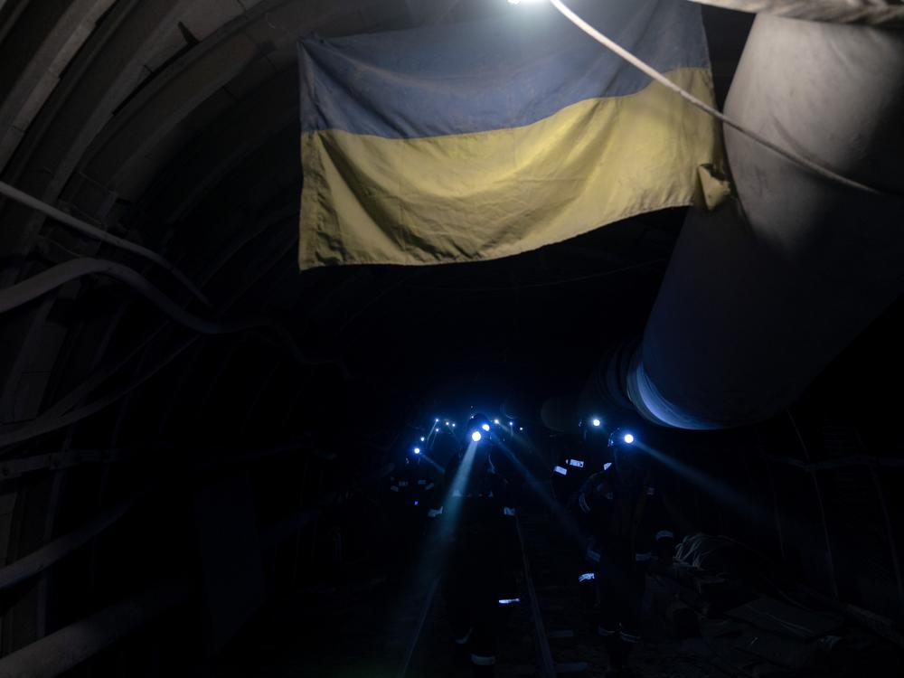Miners in the Ternivka coal mine in eastern Ukraine move through a tunnel adorned with a Ukrainian flag.