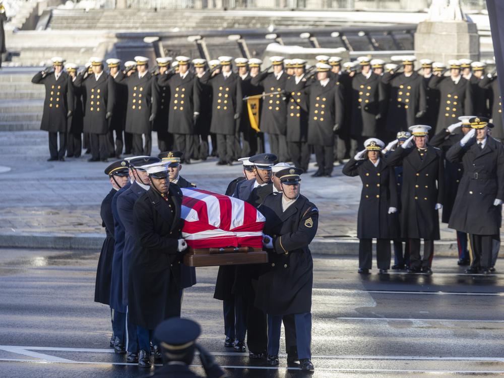 The casket of former President Jimmy Carter seen transferred from a hearse to a horse-drawn caisson to be moved down Pennsylvania Ave towards the Capitol where he will lie in state.