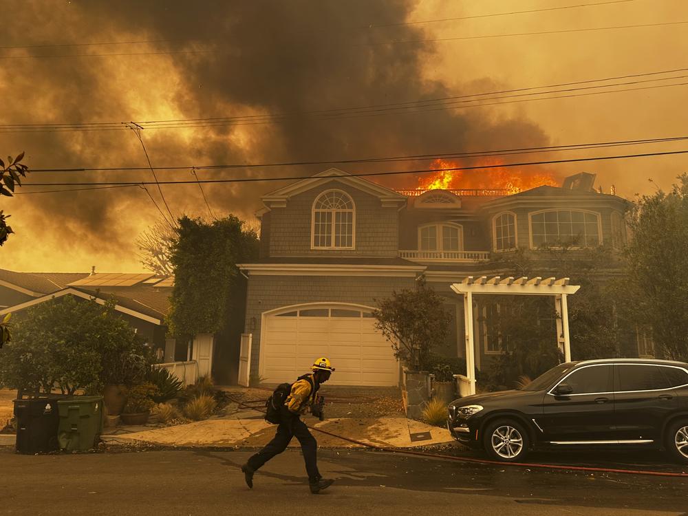 A residence burns as a firefighter battles the Palisades Fire in the Pacific Palisades neighborhood of Los Angeles.