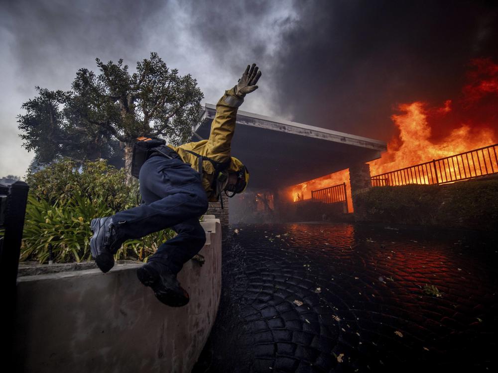 A firefighter jumps over a fence while fighting the Palisades Fire in the Pacific Palisades neighborhood of Los Angeles.