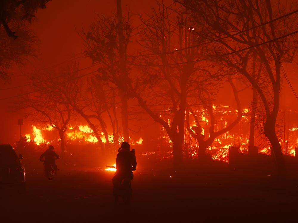 Two persons ride by on motorcycles as the Palisades Fire destroys a neighborhood in the Pacific Palisades neighborhood of Los Angeles on Tuesday, Jan. 7, 2025.