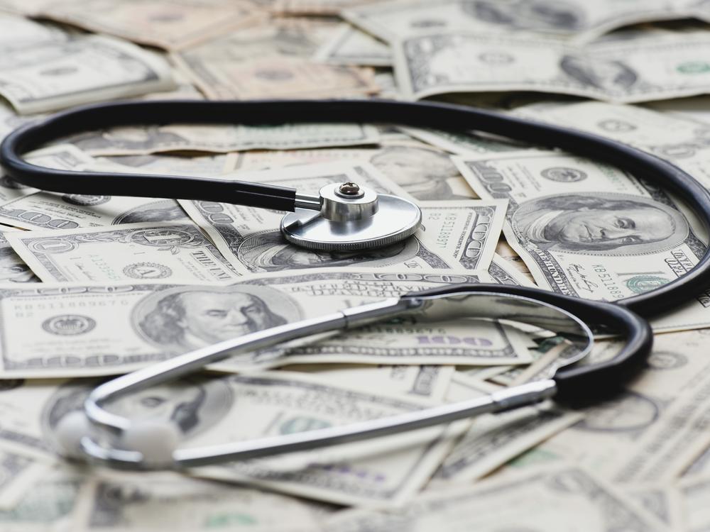 A stethoscope sits on a pile of U.S. bank notes.
