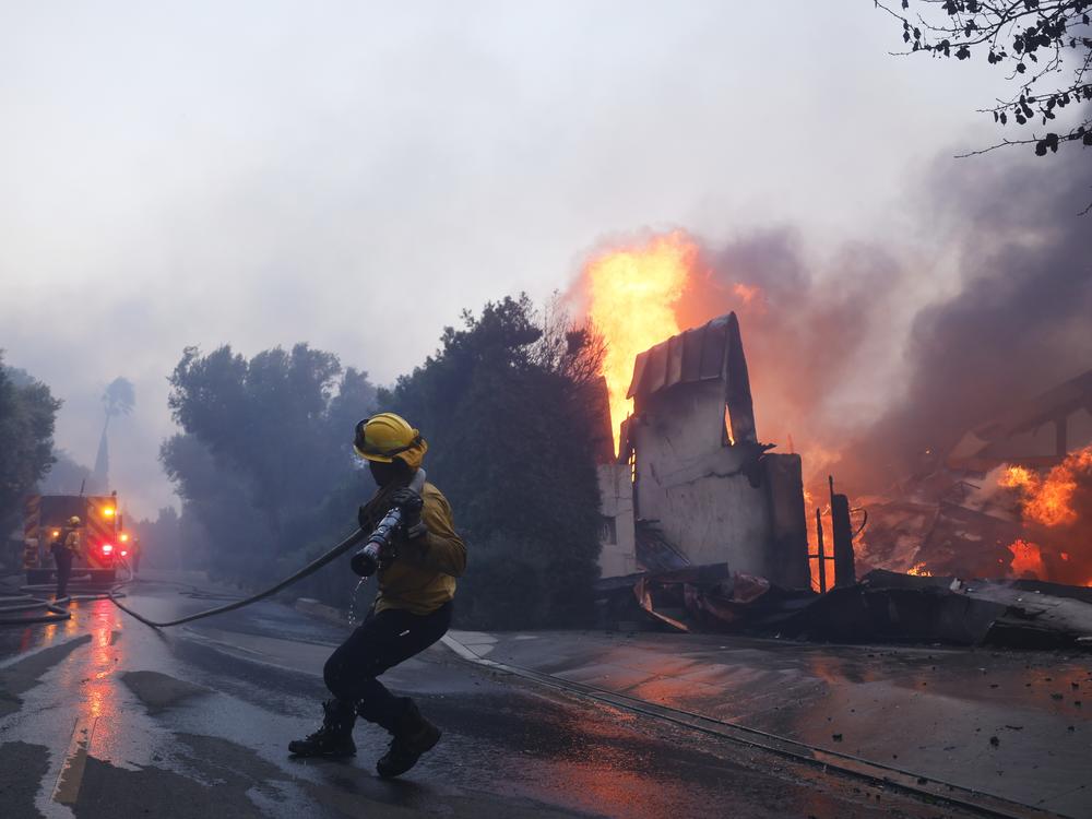 A firefighter battles the advancing Palisades Fire as it burns a structure in the Pacific Palisades neighborhood of Los Angeles on Tuesday.