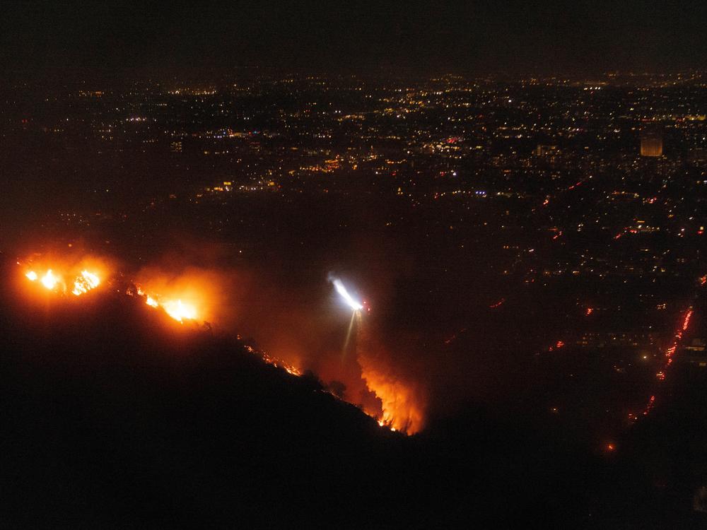 A helicopter drops water as fire burns on the Sunset Fire in the Hollywood Hills area of Los Angeles on Wednesday night.