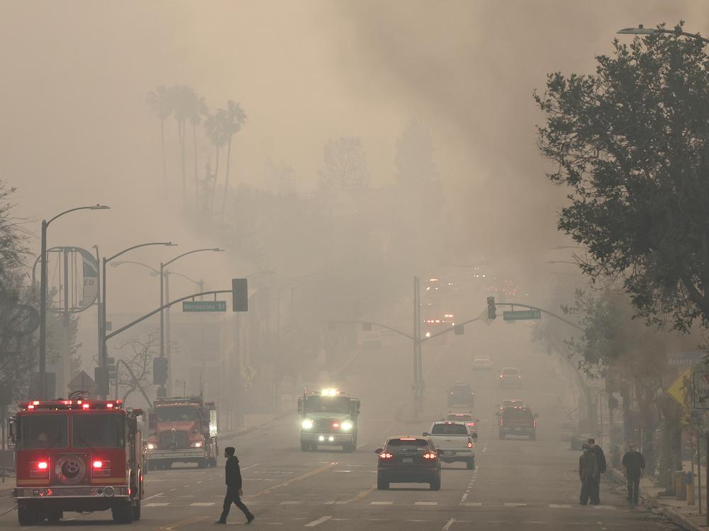 People walk through wildfire smoke in in Altadena, Calif., on Wednesday, as wildfires in Los Angeles County sharply worsened poor air quality.