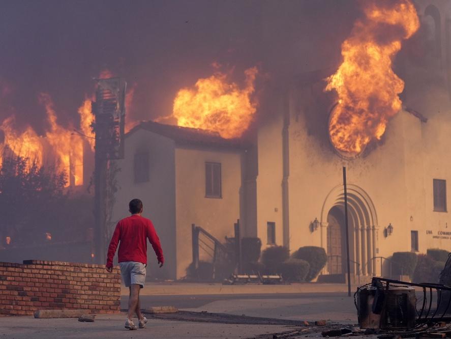 A man walks in front of the burning Altadena Community Church, Wednesday, Jan. 8, 2025, in the downtown Altadena section of Pasadena, Calif.