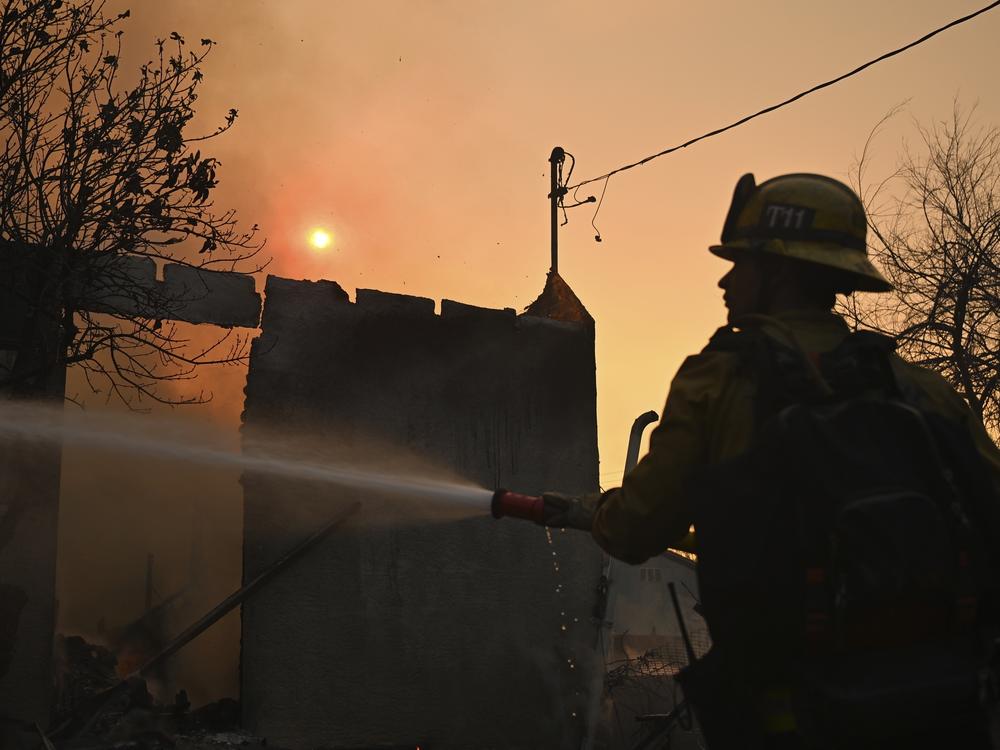 A firefighter waters down a home after the Eaton Fire burns in Altadena, Calif., Thursday, Jan. 9, 2025.
