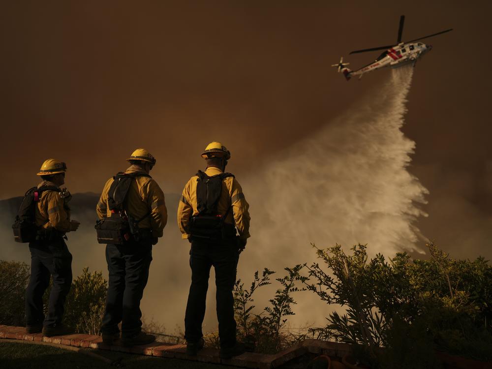 A helicopter drops water on Mandeville Canyon as the Palisades Fire rages Saturday in Los Angeles.