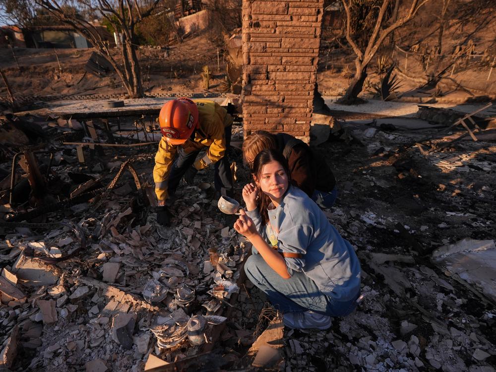 Saturday, Jan. 11: Ella Venne, front, holds a cup she found in the remains of her family's home destroyed by the Eaton Fire as she searches with Glendale Fire Department Capt. Chris Jernegan, left, and his wife, Alison, in Altadena.
