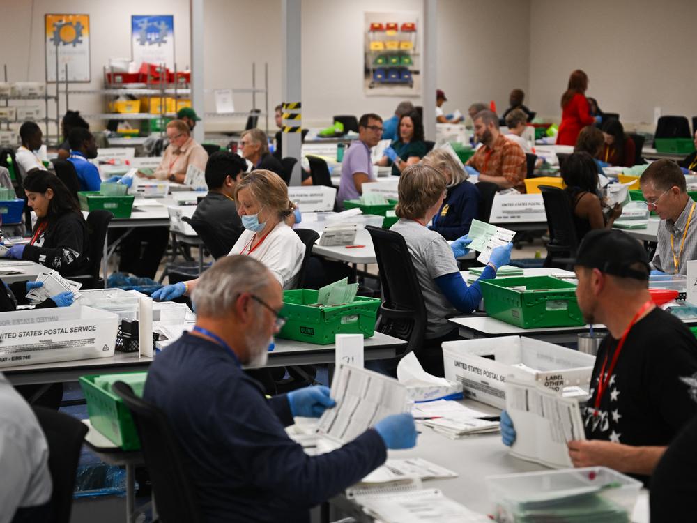 Pairs of election workers from different political parties open and inspect mail ballot envelopes inside the Maricopa County Tabulation and Election Center in Phoenix on Election Day, Nov. 5, 2024.