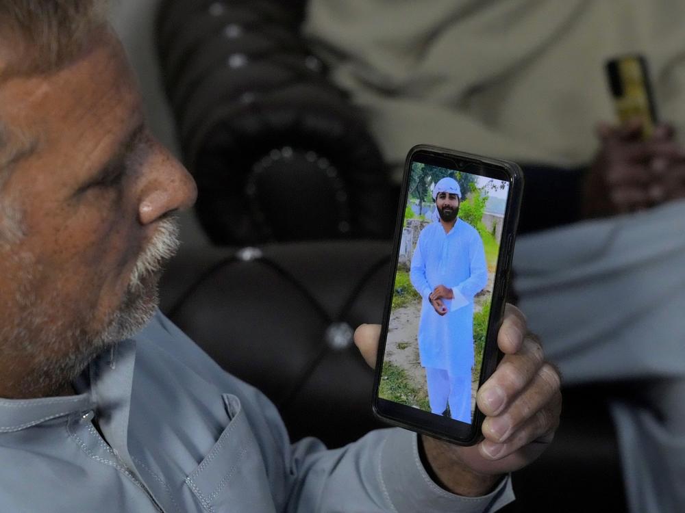 A Pakistani Mohammad Akram shows a picture of his son Abu Bakar,  one of the victims of a migrant boat that capsized in West Africa's Atlantic coastline,  on his cell phone at his home, in Jura village, in the Lalamusa district in Pakistan, on Friday.