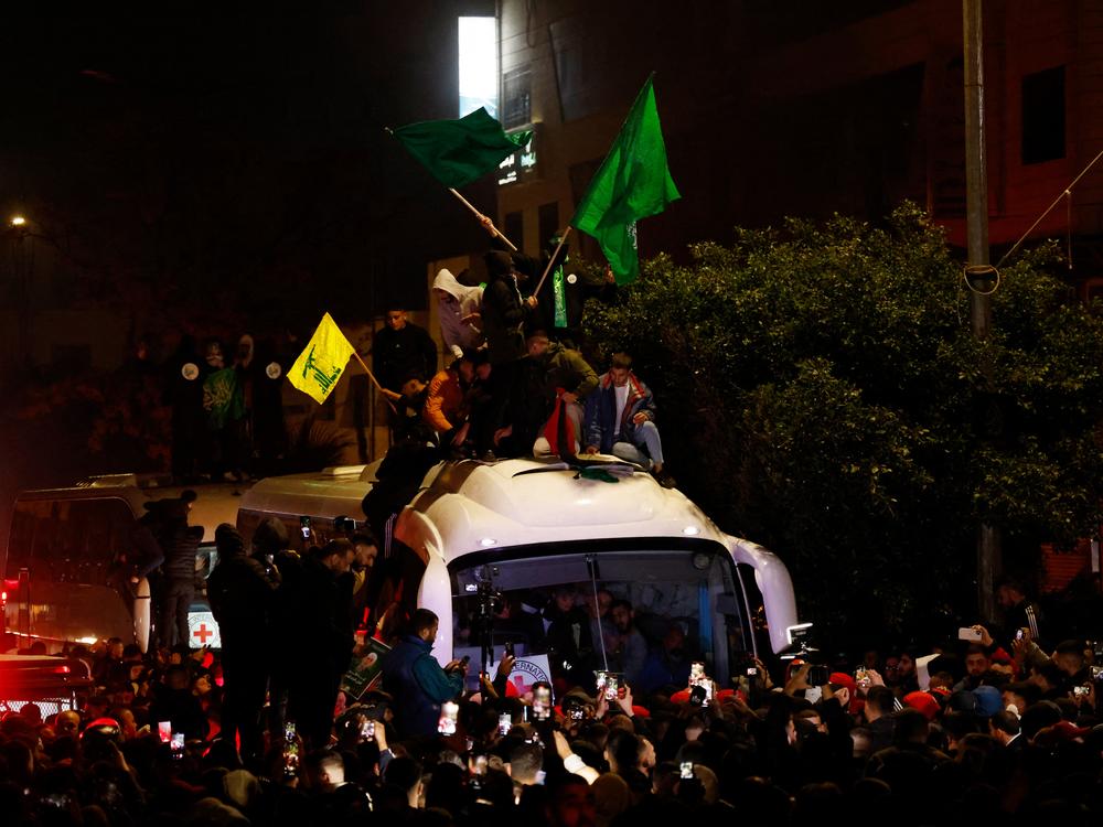 Palestinian men waving Hamas and Hezbollah flags sit on top of a Red Cross bus carrying released prisoners from Ofer military prison in the occupied West Bank are met by a crowd of family members and friends in Beitunia, outside Ramallah, in the early hours of Jan. 20, 2025.