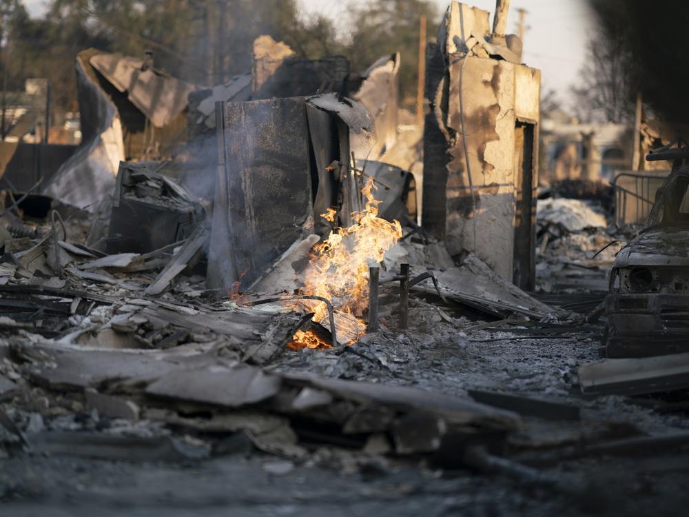 Some gas lines were still burning in Altadena, California, after the Eaton fire passed through a burned neighborhood. Crews were working to cut off gas to the area. Smoke and ash from the LA-area fires blanketed the region. Experts suggest care while cleaning up, even far from the immediate burn zones.