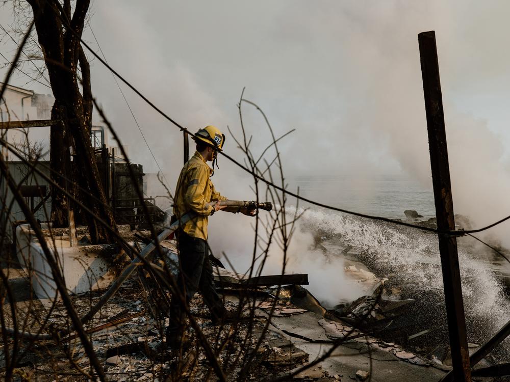 A firefighter works with water hoses near houses burned down in the Palisades Fire along the Pacific Coast Highway in Malibu, Calif. on Jan. 9, 2025.