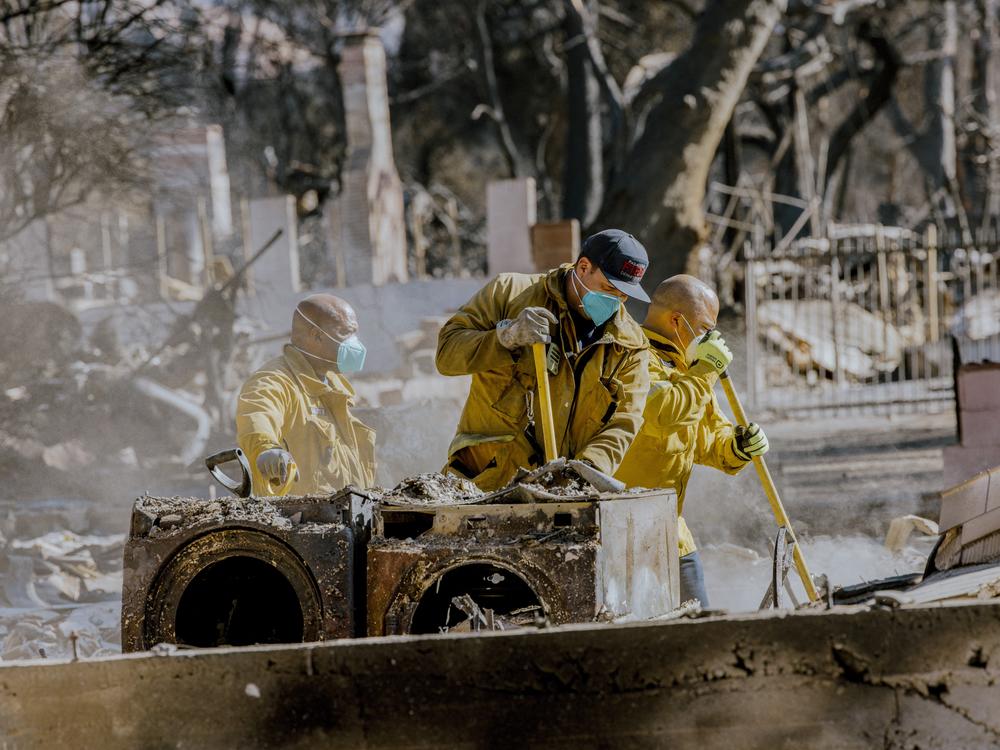 Firefighters clean up after the Eaton Fire in California. Health experts recommend wearing particle-filtering masks, goggles, gloves, and other personal protective equipment while cleaning up the potentially toxic ash and smoke after the burn.