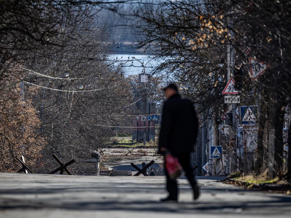 A man walks down a street in the front-line city Kherson, where traffic is blocked by anti-tank hedgehogs. The Dnipro River can be seen in the background. That's the front line. Russian drone pilots and artillery crews operate from the far bank in clear sight of neighborhoods that are home to at least 60,000 civilians.