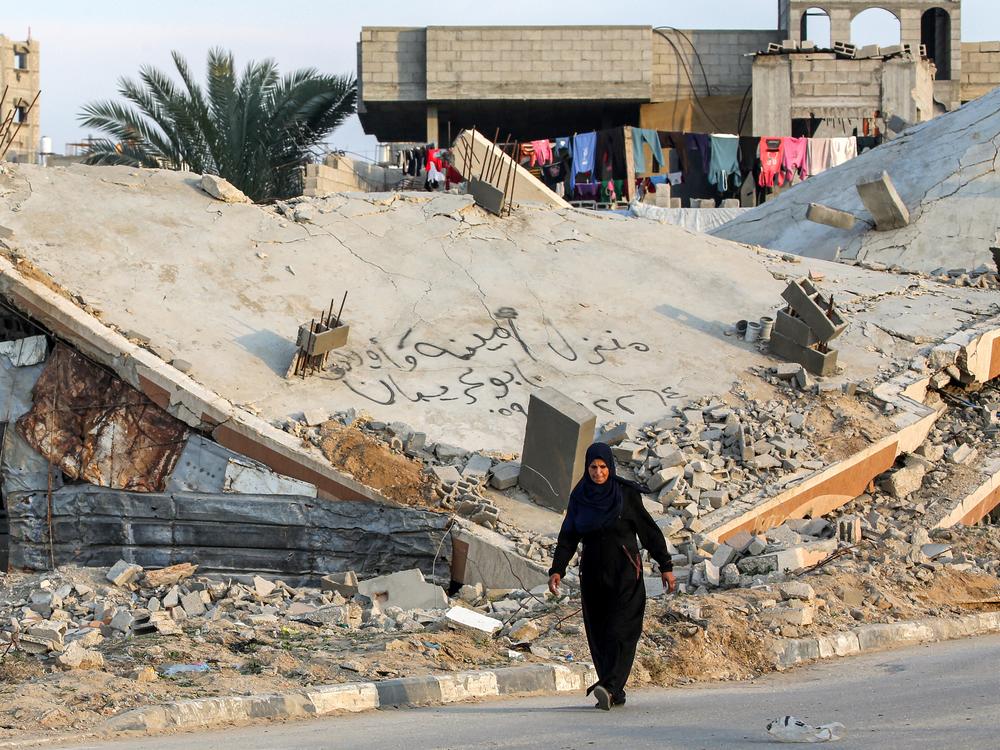 A woman walks past the rubble of a collapsed building at a camp for people displaced by conflict in Bureij, in the central Gaza Strip, on Jan. 17, following the announcement of a truce amid the war between Israel and Hamas.