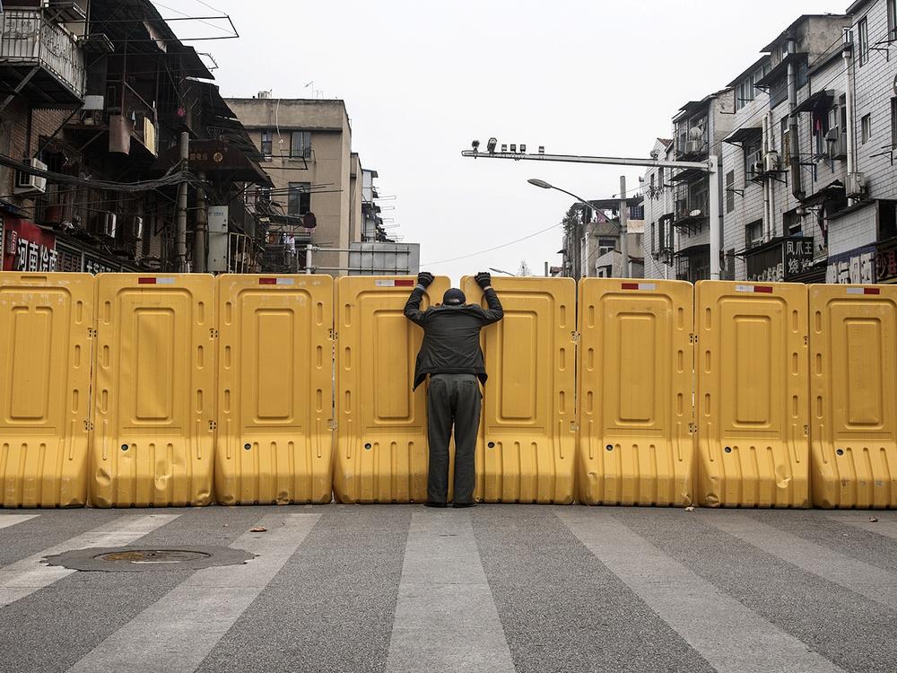 One man talks to another man on March 8, 2020, through a makeshift barricade wall built to control entry and exit to a residential compound in Wuhan, Hubei, China.