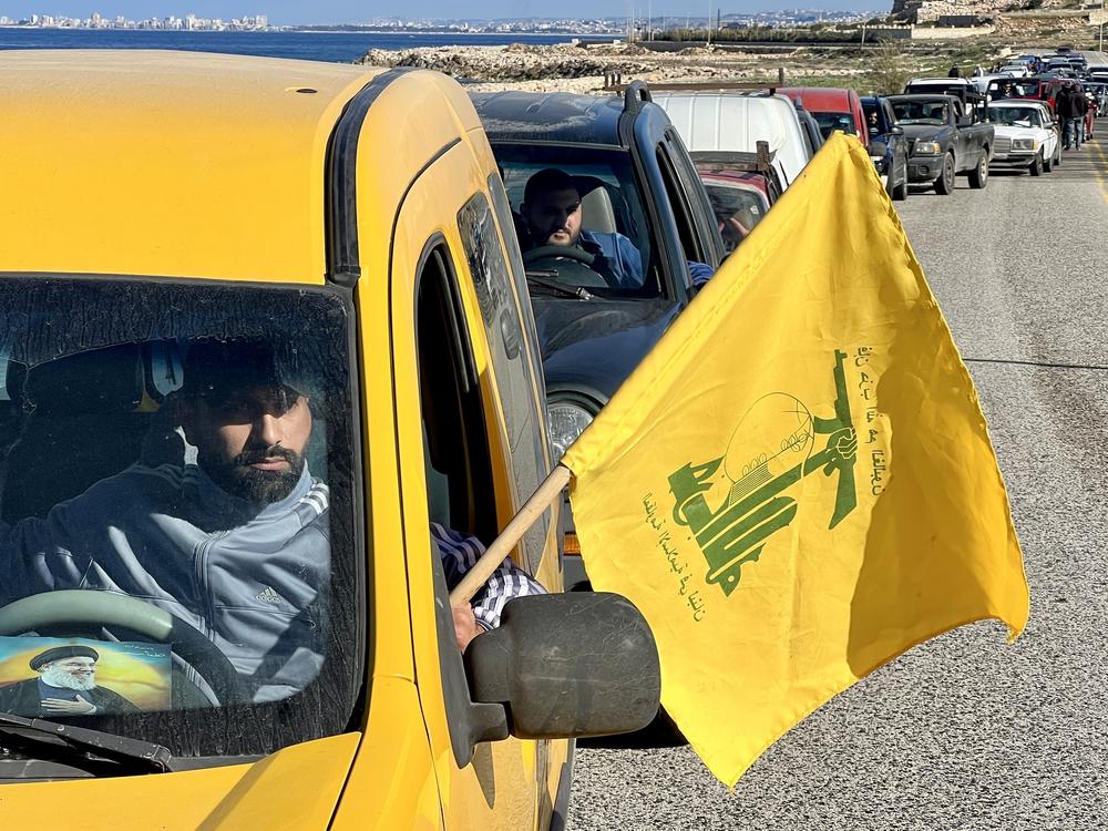 A man carries the Hezbollah flag and drives a car with a photo of the militant group's former leader, Hassan Nasrallah, on the windshield, as Lebanese citizens return to their homes after Israeli forces withdraw from the area in An-Naqoura, Lebanon, on Thursday.