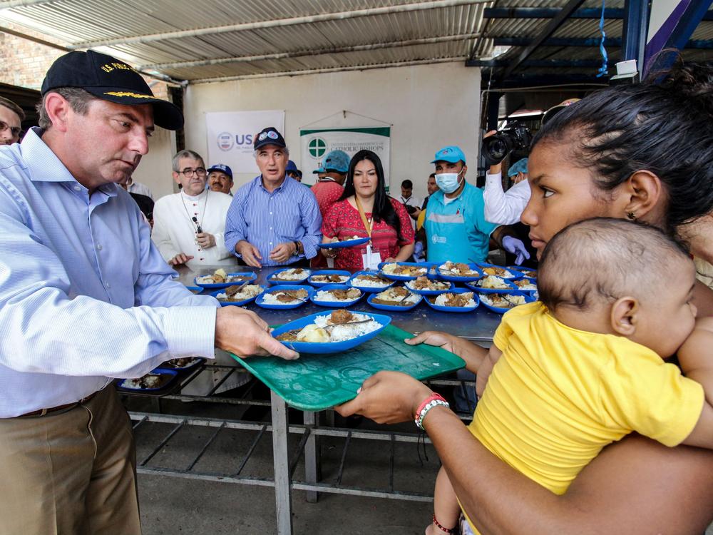 U.S. Health and Human Services Secretary Alex Azar distributes a meal to a Venezuelan migrant woman at the Migrant Assistance Center in Cucuta, Colombia.  Health officials of 11 countries of the American continent — including Azar — agreed to create a unique vaccination card for Venezuelan migrants.