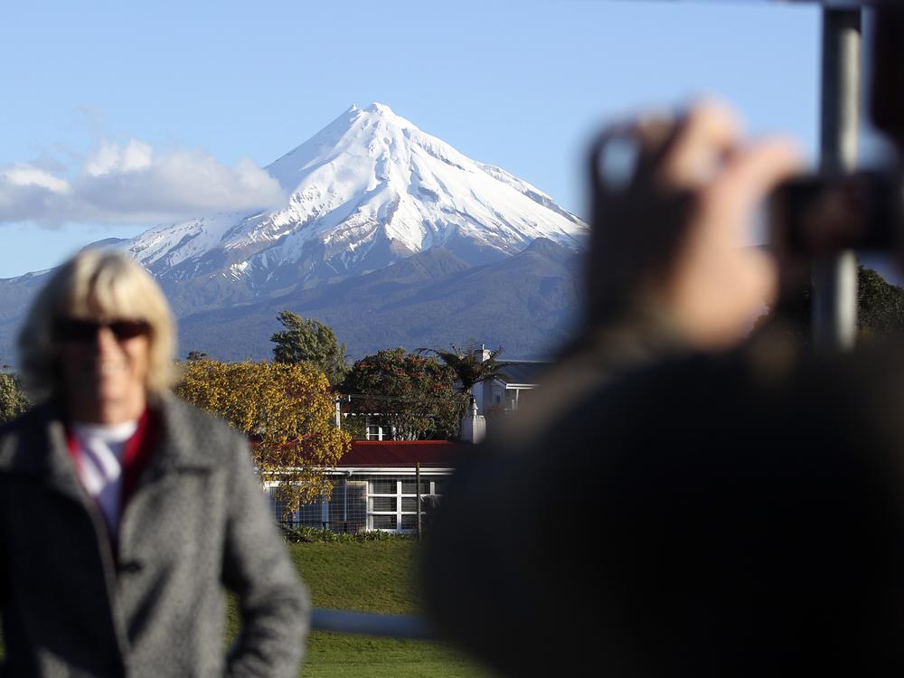 A man takes a picture of his wife with Mount Taranaki, also known as Mount Egmont, in the background in New Plymouth, New Zealand.