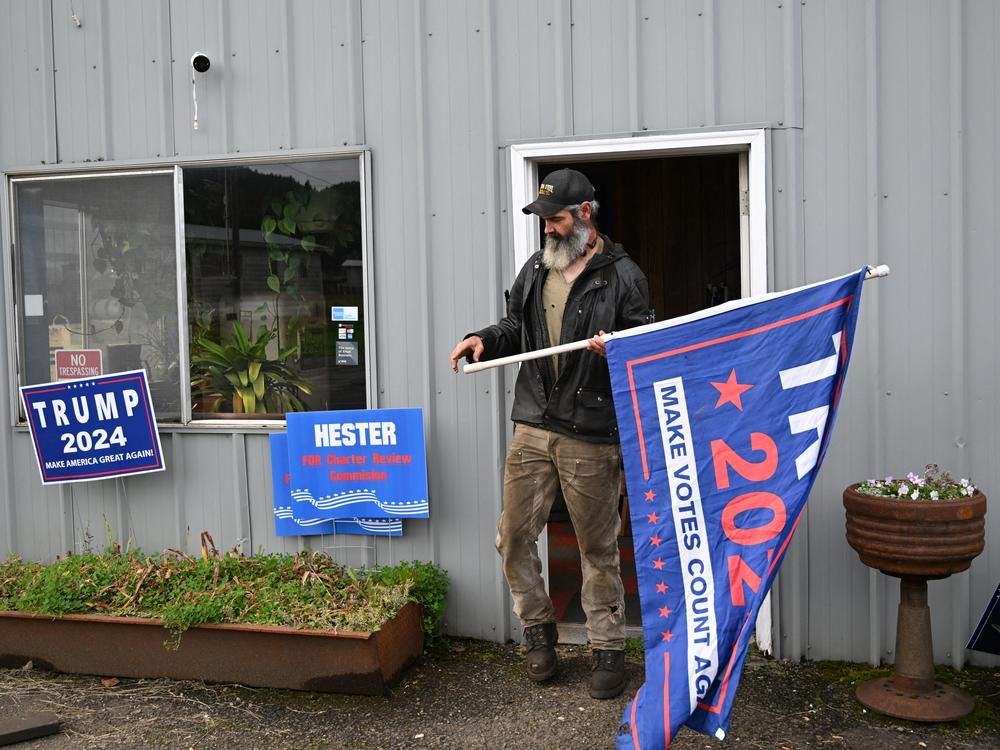 Hickory Grant, a machinist and a member of the Forks town council, unfurls a Trump flag at his workshop in Forks, Wash., on Oct. 15, 2024 in Clallam County.