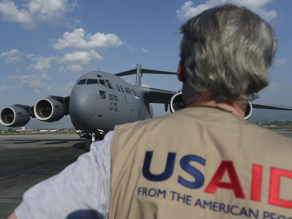 A USAID officer watches as a U.S. military cargo plane taxis to a stop at Kathmandu's international airport in the wake of the 2015 earthquake. The agency funds projects that aim to alleviate poverty and disease and meet humanitarian needs around the world.