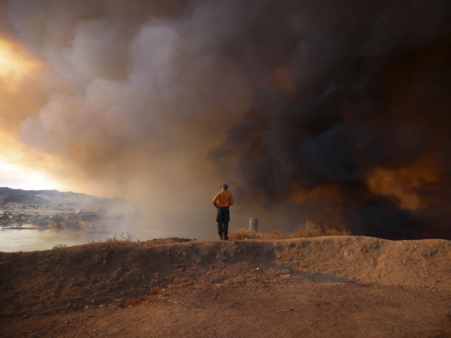 A firefighter looking out towards Lake Castaic stands on a mound backdropped by clouds of smoke caused by the Hughes Fire in Castaic, Calif., Wednesday, Jan. 22, 2025.