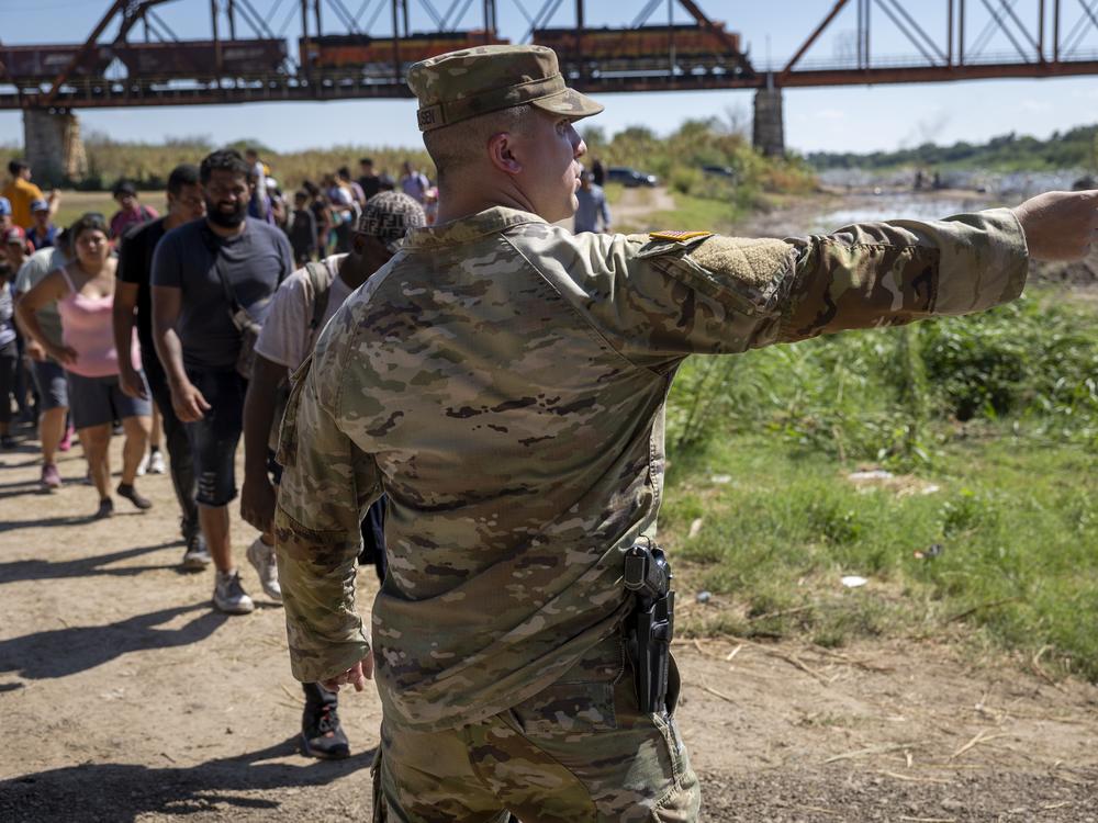 A Texas National Guard soldier directs immigrants towards a U.S. Border Patrol checkpoint after they crossed the U.S.-Mexico border in September 2023 in Eagle Pass, Texas.
