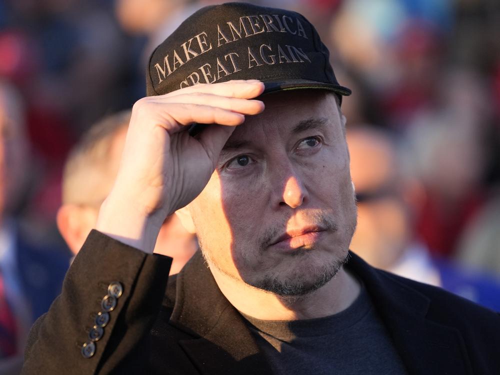 Elon Musk listens as Republican presidential nominee former President Donald Trump speaks at a campaign event at the Butler Farm Show in Pennsylvania, on Oct. 5, 2024.