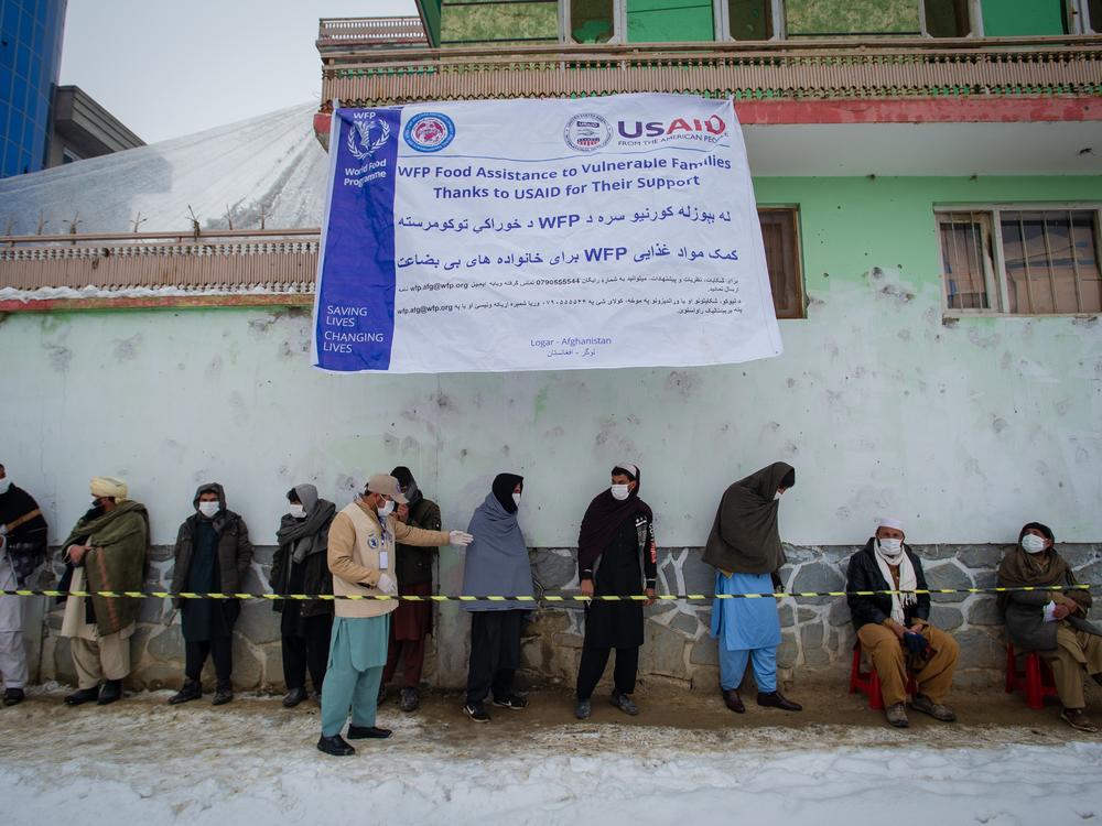 Afghan men wearing masks to prevent the spread of COVID-19 line up as the U.N.'s World Food Program (WFP) distributes a monthly food ration to address fears of looming famine due to drought and winter conditions. Food for this delivery in January 2022 was largely supplied by the U.S. Agency for International Development (USAID).