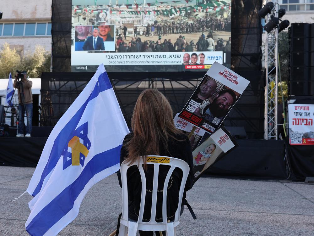 A woman sits on a char in front of a screen in Tel Aviv's Hostages Square, holding an Israeli flag and pictures of hostages as families wait on Feb. 15, 2025, for the release by Hamas of three double-nationals held in the Gaza Strip since the Oct. 7, 2023.