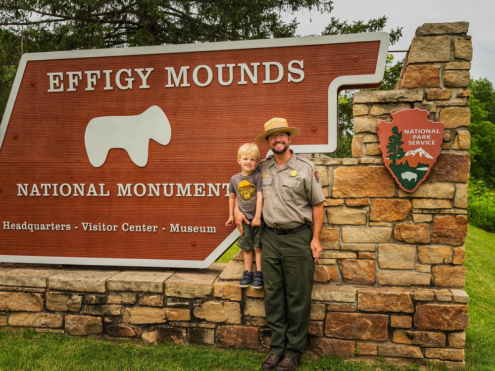 Brian Gibbs, pictured with his son Oliver in front of the Effigy Mounds National Monument park sign, in July 2024.