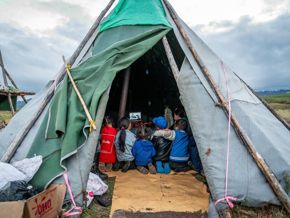 Children gather inside a traditional tent, known as an ortz, in the Siberian taiga of northern Mongolia, watching a documentary about a Norwegian reindeer herder who was visiting the taiga to meet and learn about the lifestyle of the region's nomadic Dukha reindeer herders. Despite its remote and isolated location deep in the forest - accessible only by horseback or reindeer - modern technology such as solar panels, car batteries, and occasional wifi connection, allows these families to stay connected with…
