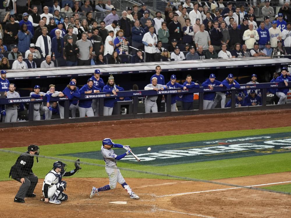 Los Angeles Dodgers' Mookie Betts, right, hits a sacrifice fly as New York Yankees catcher Austin Wells, center, reaches for the pitch during the eighth inning in Game 5 of the World Series, Oct. 30, 2024, in New York.