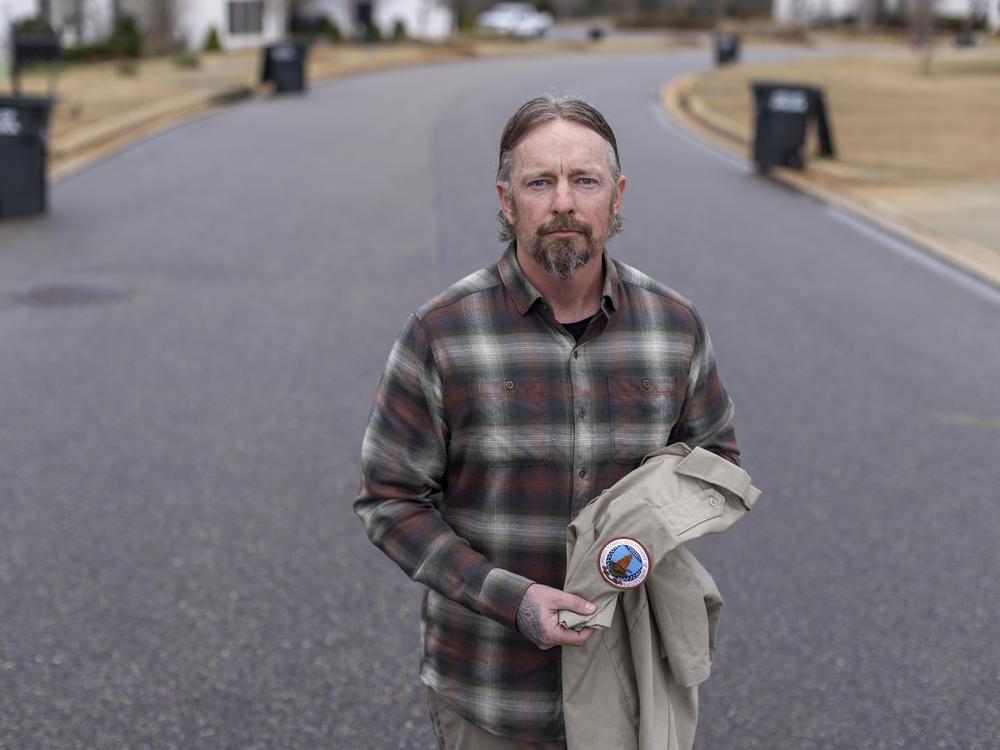 Derek Copeland, who was recently fired from the U.S. Department of Agriculture, holds a USDA work shirt near his residence in Opelika, Alabama. The Air Force veteran had worked as a dog trainer for the USDA.